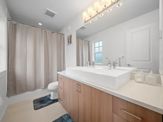 Modern bathroom featuring a double vanity with an integrated rectangular sink, light wood-finish cabinetry, and a white countertop