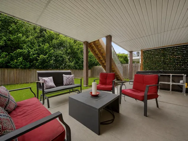Covered concrete patio featuring a slatted ceiling, wood privacy fence, and a staircase with wood treads and metal balusters