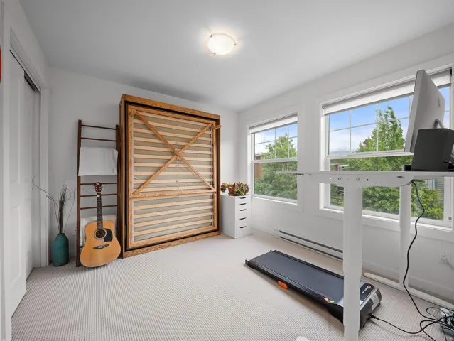 Versatile room featuring a built-in wood-frame Murphy bed, two large windows with roller shades, and light-toned carpet flooring
