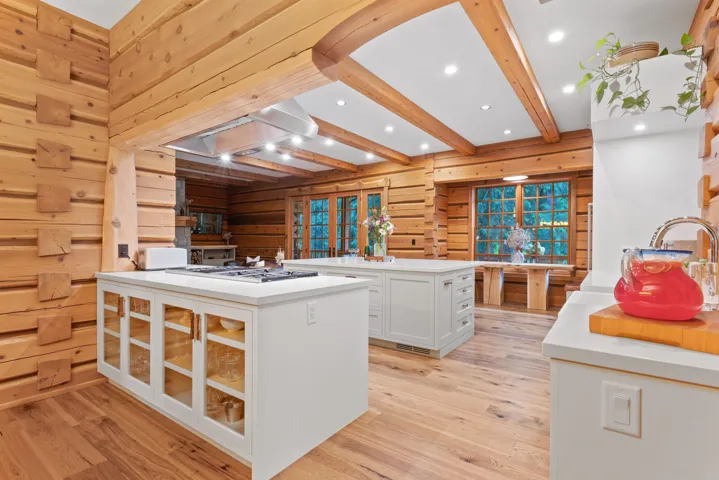 Kitchen with wood walls, stainless steel gas cooktop, beamed ceiling, white cabinetry, and light wood-style flooring