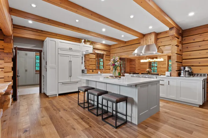 Kitchen featuring a breakfast bar area, light countertops, beamed ceiling, paneled built in fridge, and wooden walls