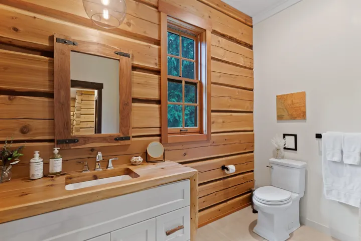 Half bath featuring tile patterned flooring, wood walls, baseboards, vanity, and toilet