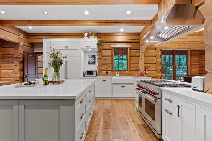 Kitchen with range with two ovens, range hood, wood walls, light wood finished floors, and white cabinetry