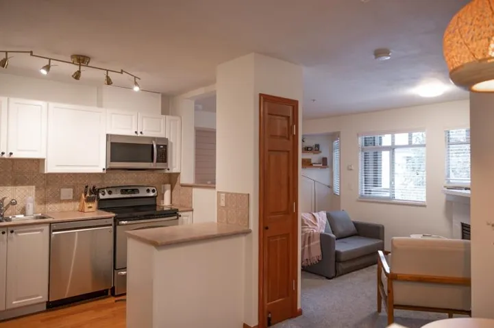 Contemporary kitchen featuring white cabinetry, stainless steel appliances, patterned tile backsplash, wood-finish flooring, and track lighting