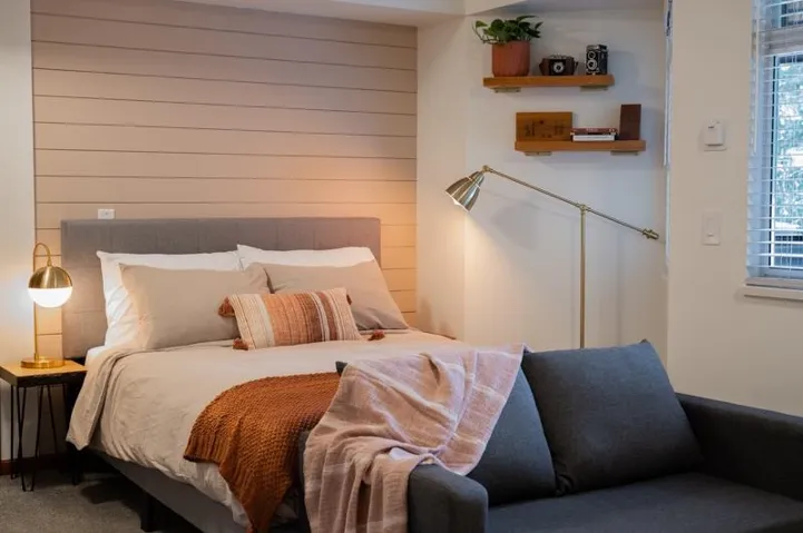 Bedroom featuring a shiplap accent wall, two wall-mounted wood shelves, a window with blinds, and carpeted flooring
