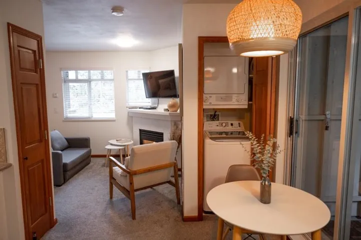 Living area featuring a white mantel fireplace, two windows with blinds, a built-in stacked washer and dryer, and a sliding glass door