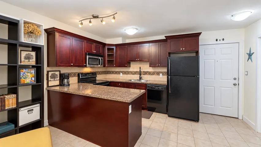 Kitchen featuring rich wood-finish cabinetry, granite-style countertops, black appliances, tile flooring, and track lighting