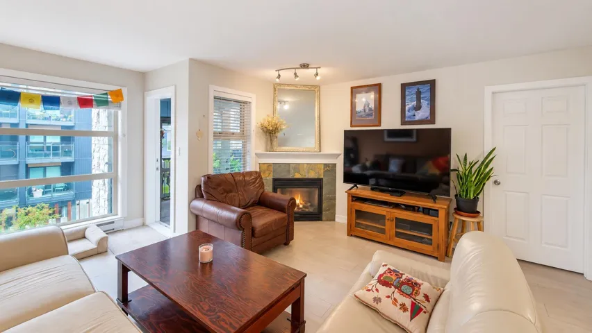 Corner fireplace with stone surround and mantle, large window, and wood-finish flooring