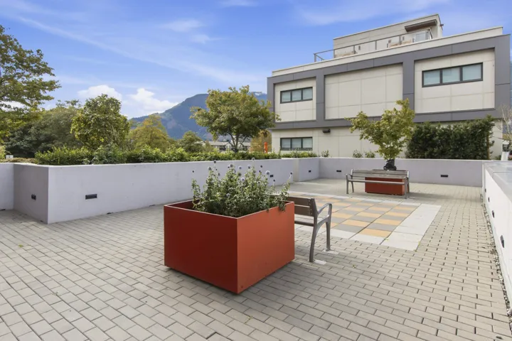 Expansive rooftop patio featuring paver flooring, integrated benches, raised planters, a decorative checkered tile inset, and a perimeter wall