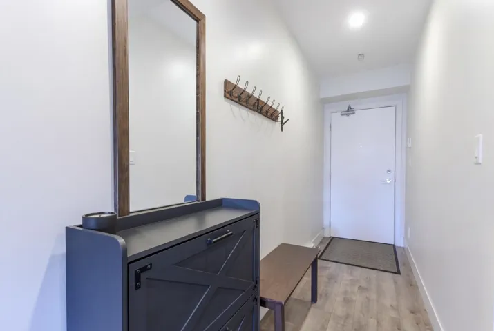 Entryway featuring light wood-finish flooring, a wall-mounted mirror with a wood frame, and a built-in coat rack