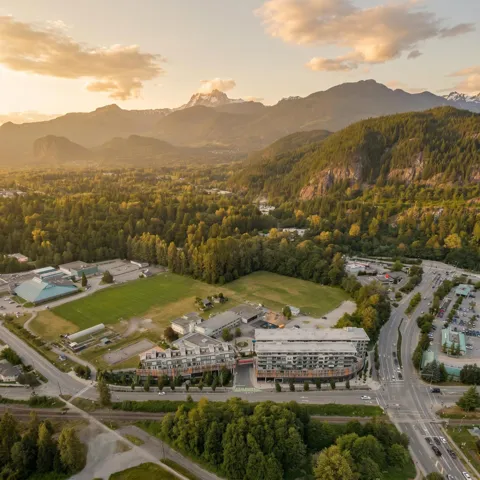 Aerial perspective showcasing mountain scenery, extensive tree coverage, multiple residential buildings, a sports field, and roadways