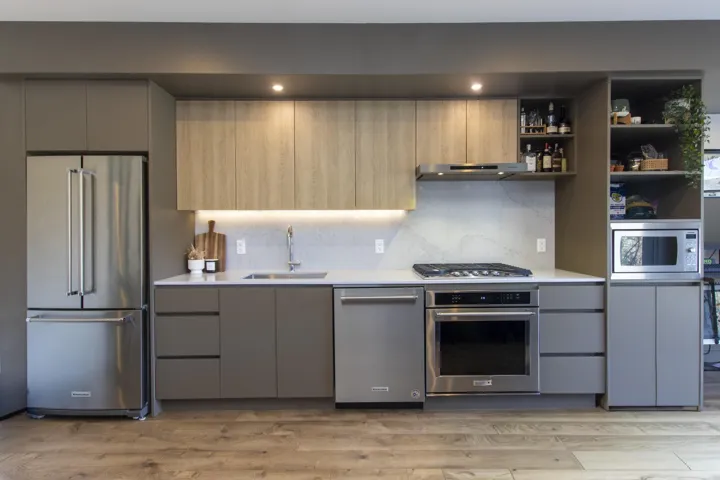 Contemporary kitchen featuring wood-finish flooring, integrated stainless-steel appliances, sleek flat-panel cabinetry, under-cabinet lighting, and stone countertops with a matching backsplash