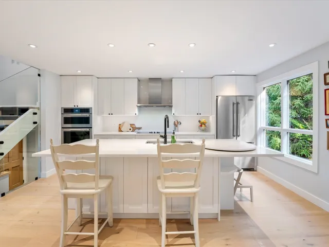 Kitchen featuring a sink, wall chimney range hood, appliances with stainless steel finishes, a center island with sink, and light wood-style flooring