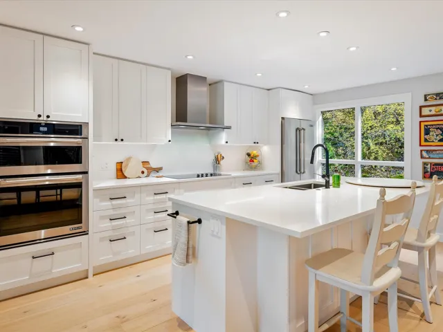Kitchen with a sink, wall chimney range hood, light wood finished floors, a center island with sink, and stainless steel appliances