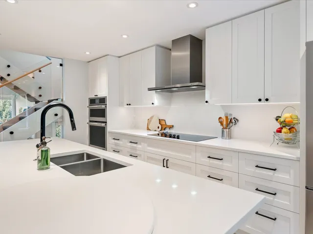 Kitchen with light countertops, a sink, wall chimney exhaust hood, and white cabinetry