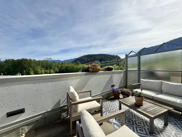 Expansive outdoor patio featuring a concrete perimeter wall, a privacy screen, and a mountain and forest backdrop