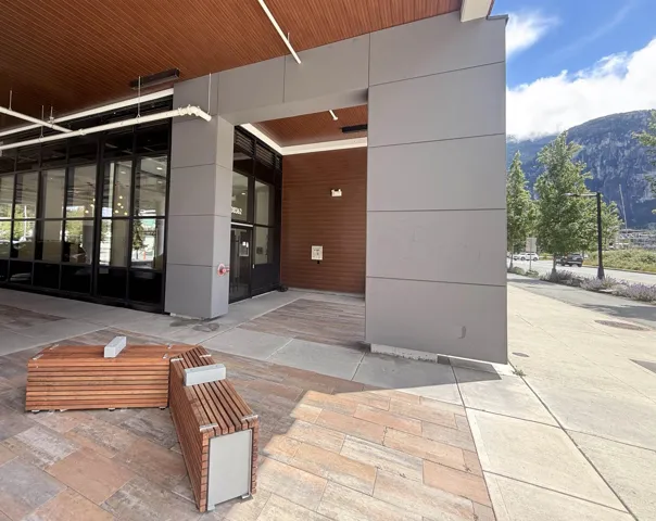 Modern building entrance featuring a wood-panel ceiling, full-height windows, and a grey paneled exterior