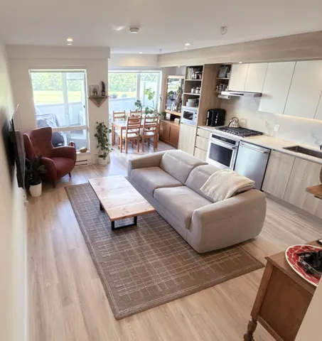 Open-concept living space featuring wood-finish flooring, recessed lighting, a modern kitchen with integrated appliances, and a dining area with direct access to a private patio