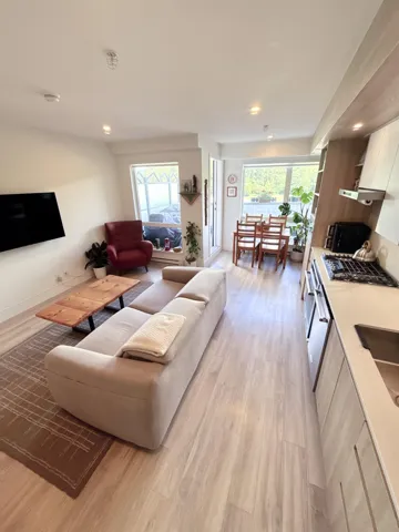 Open-concept living area featuring light wood-finish flooring throughout, recessed ceiling lighting, a contemporary kitchen with light-toned cabinetry, and ample natural light from multiple windows