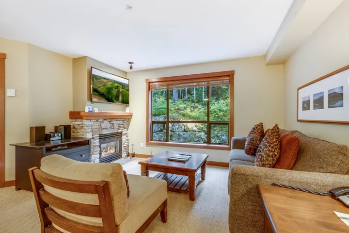 Carpeted living area with a stone fireplace and baseboards