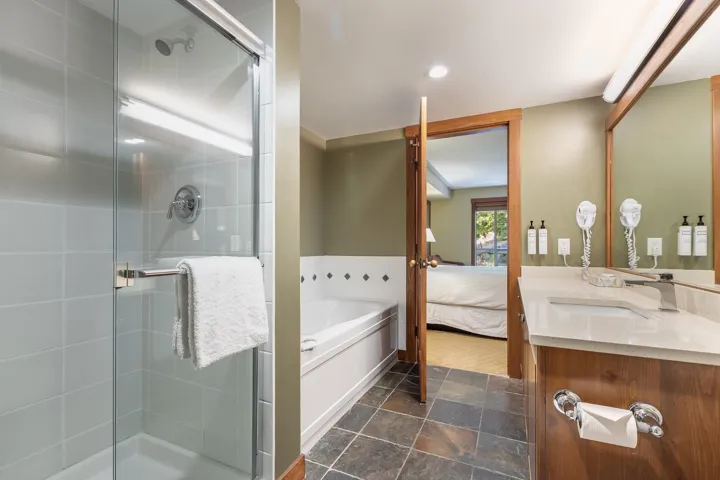 Ensuite bathroom featuring vanity, a shower stall, a garden tub, and dark stone finish floors