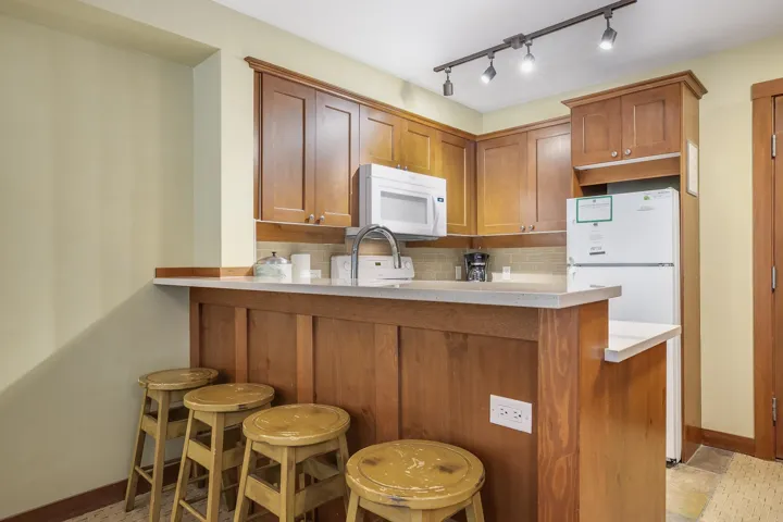Kitchen featuring backsplash, brown cabinetry, a breakfast bar, light countertops, and white appliances