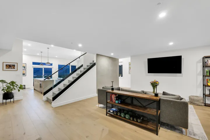 Open-concept living area featuring light wood-finish flooring, recessed lighting, and a contemporary glass railing staircase with dark banisters