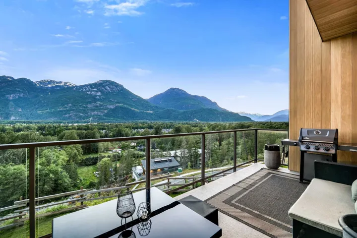 Expansive outdoor balcony featuring glass railings, natural wood paneling, and a concrete floor