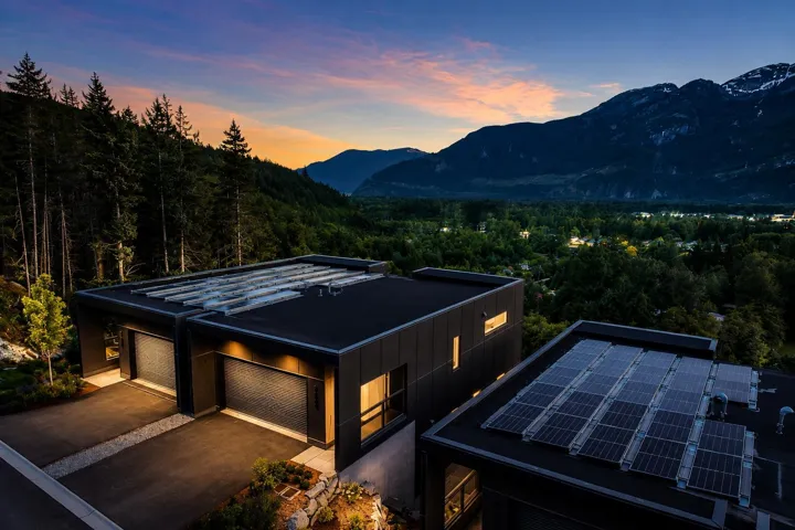 Contemporary architectural design featuring dark exterior cladding, multiple garage bays, and solar panel arrays