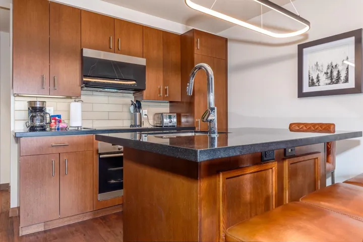 Kitchen with brown cabinets, backsplash, dark stone countertops, stainless steel oven, and dark wood finished floors