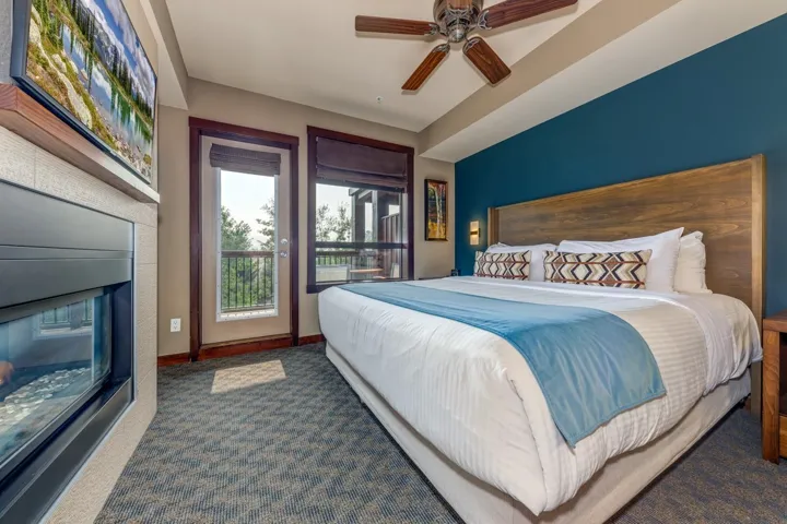 Carpeted bedroom featuring a ceiling fan, a glass covered fireplace, and access to outside