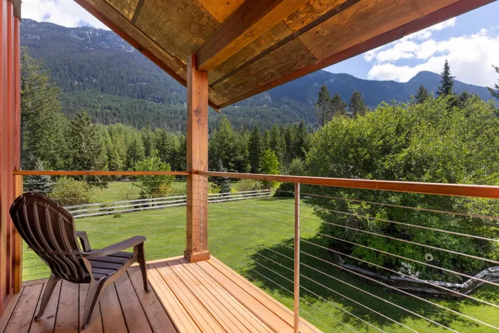 Wood-plank balcony with cable railing, offering expansive views of a verdant landscape and distant mountains