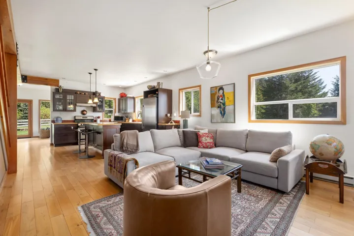 Open-concept living space featuring wood-finish flooring, a kitchen island with seating, stainless steel appliances, and large windows with wood trim