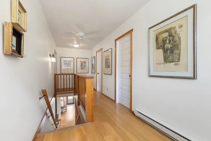Upper-level hallway featuring wood-finish flooring, white paneled doors with wood trim, and a built-in ceiling fan with lighting