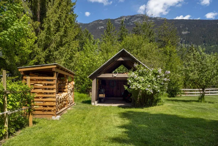 Gable-roofed open-air structure and separate wood storage shed on a grassy yard