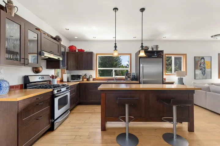 Contemporary kitchen featuring rich wood cabinetry, light wood-finish countertops, stainless steel appliances, and a central island with pendant lighting