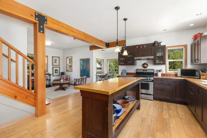 Bright kitchen featuring wood-finish flooring, dark wood cabinetry, stainless steel appliances, and a central island with a light wood-finish countertop