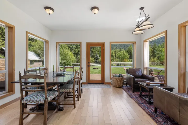 Open-concept living space featuring light wood-finish flooring, multiple large windows with wood trim, a wood-frame glass panel door, and recessed ceiling lighting