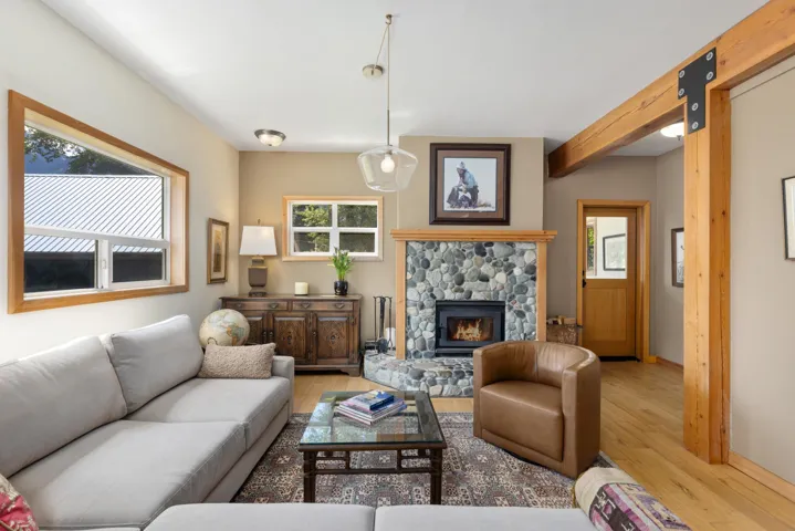 Living area featuring a stone-faced fireplace with a wood mantel, exposed wood beam accents, and wood-finish flooring