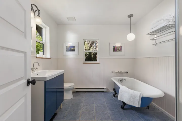 Bathroom featuring a clawfoot tub, blue vanity with an integrated sink, floor-to-ceiling wainscoting, and tile flooring