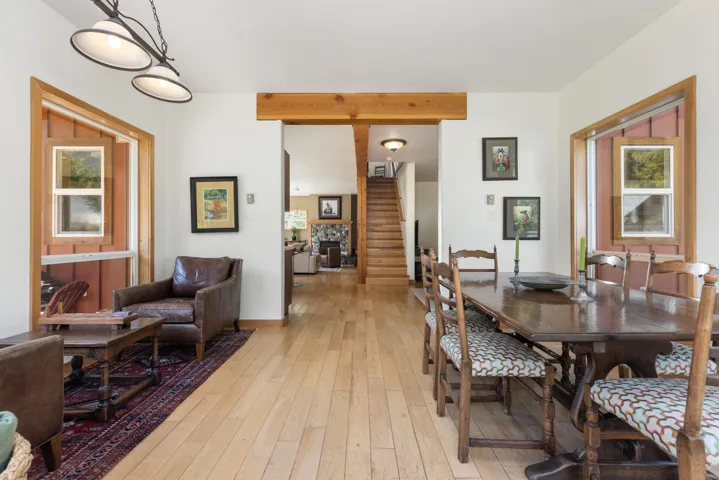 Open-concept interior featuring light wood-finish flooring, a prominent wood beam, and wood-framed windows