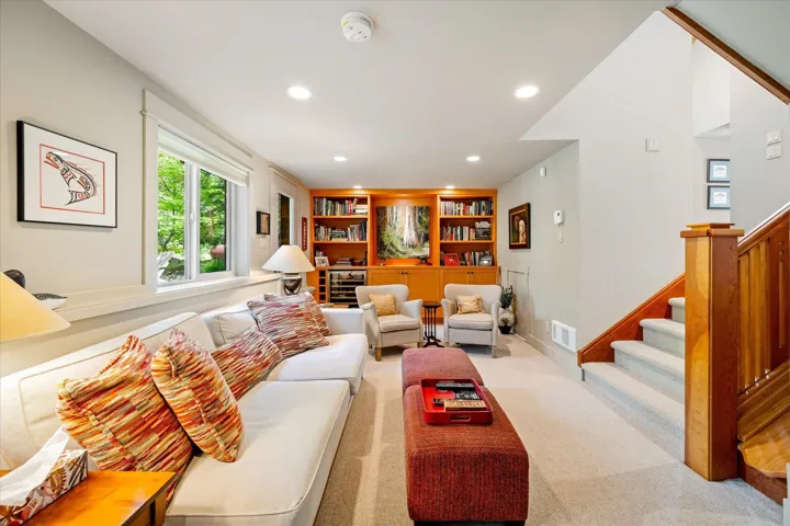 Spacious room featuring light carpeting, recessed lighting, a built-in wood-finish shelving unit, a double window, and a wood-finish staircase with carpeted treads