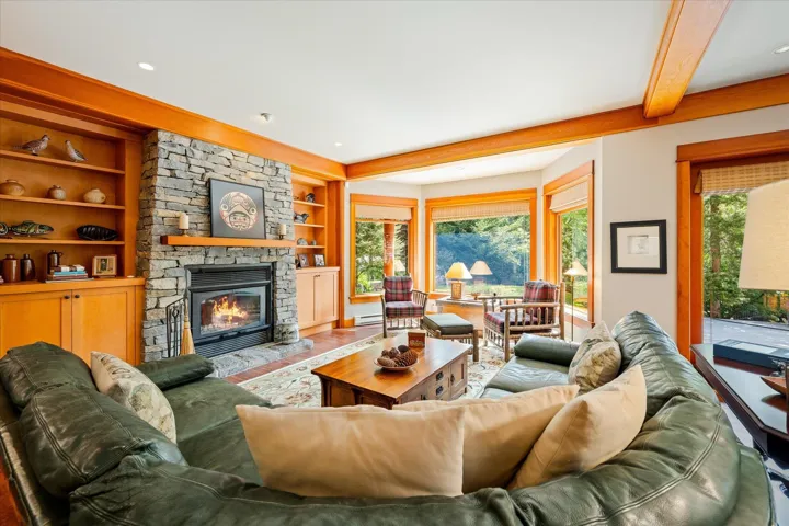 Living area featuring a stone-clad fireplace and wood mantle, built-in shelving with lower cabinetry, and exposed wood beams