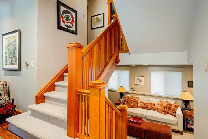 Craftsman-style wooden staircase with light-colored carpeted treads, complemented by a recessed seating area featuring two windows with white blinds