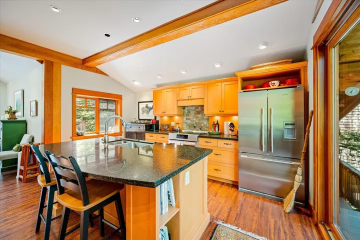 Kitchen featuring a substantial island with countertop seating, stainless steel appliances, wood-finish flooring, vaulted ceilings with exposed wood beams, and ample cabinetry
