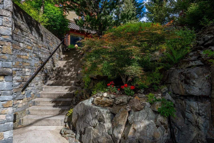 Stone staircase with a black metal handrail, bordered by a multi-tone stone retaining wall and natural rock outcroppings