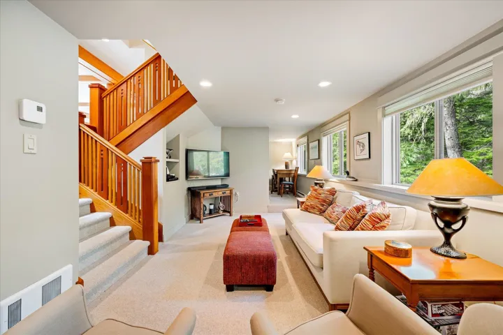 Carpeted living area featuring a wooden staircase with balusters, recessed lighting, and multiple windows