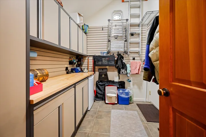 Utility space with slatwall organization system, extensive cabinetry, wood-finish countertop, and durable tile flooring