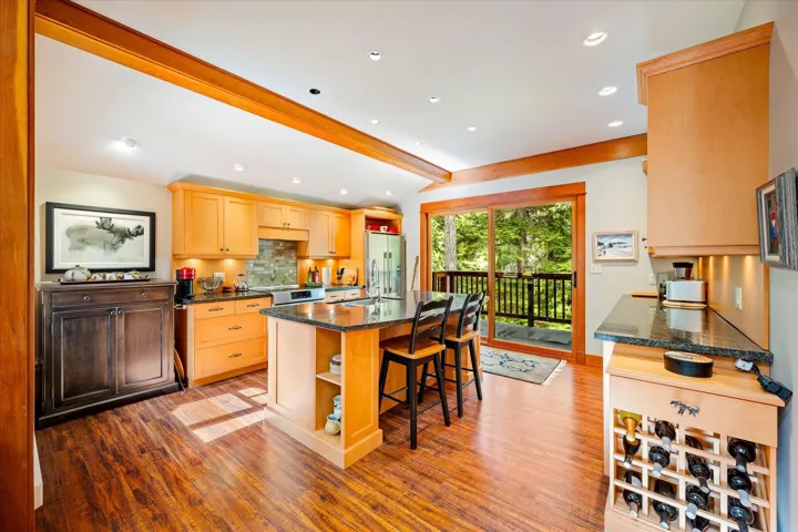 Kitchen featuring wood-finish flooring, light-toned cabinetry, a central island with countertop seating, recessed ceiling lighting, and glass sliding doors opening to an outdoor deck