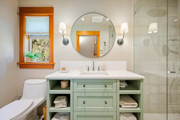 Modern bathroom featuring a sage green vanity with open shelving and drawer storage